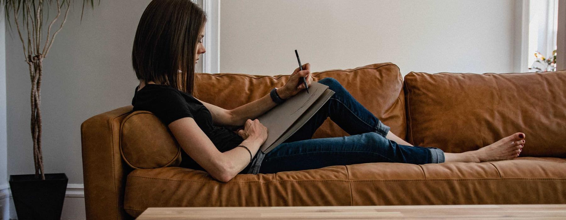 woman lies on a couch and draws on a large sketch pad